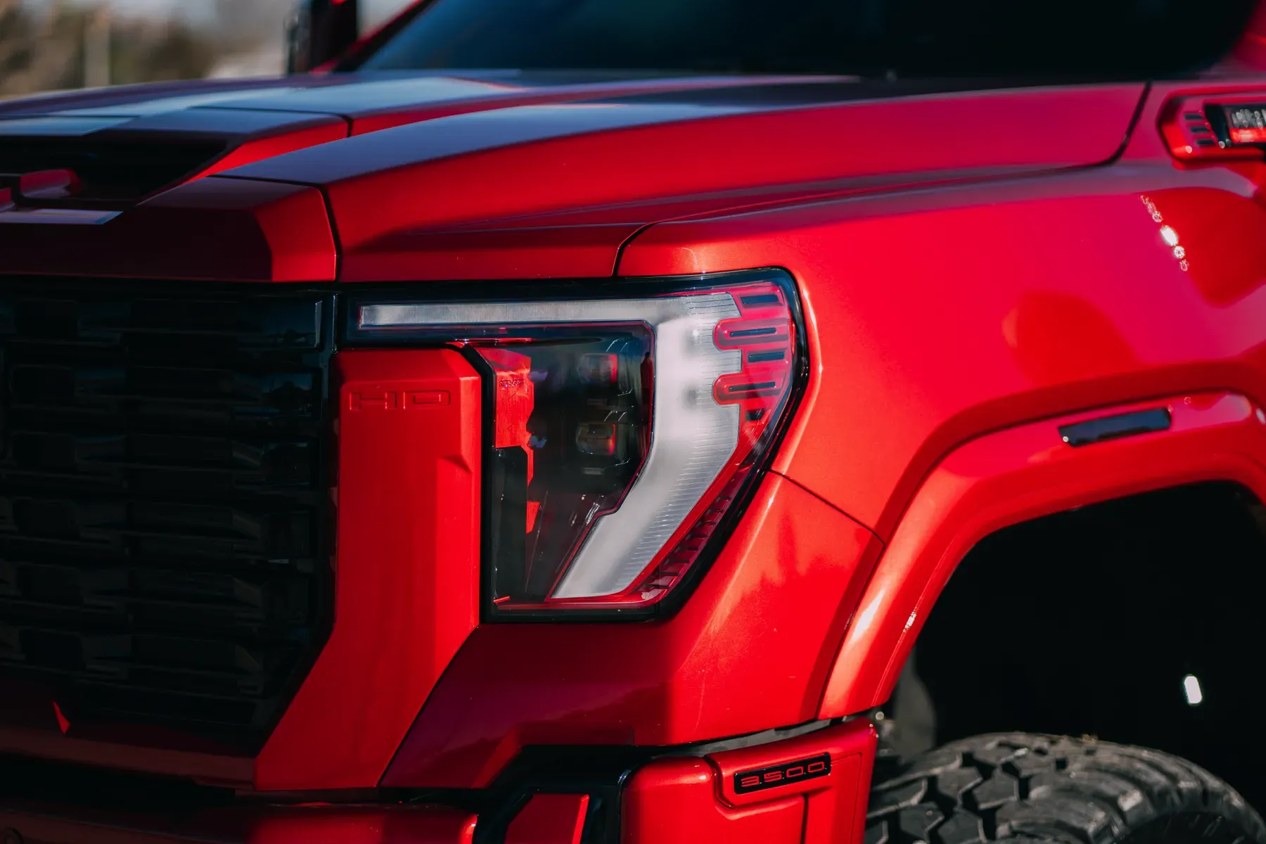 Close-up of the distinctive headlights and grille of a vibrant red GMC Sierra pickup truck.