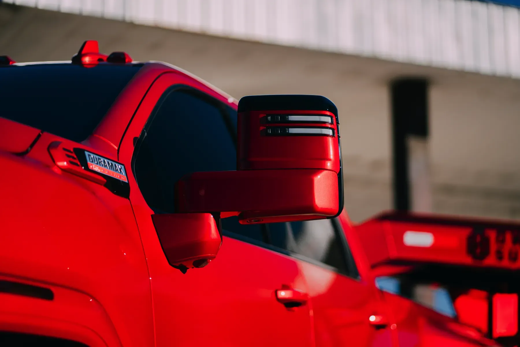 Close-up of a bright red truck's side mirror with integrated LED turn signals.