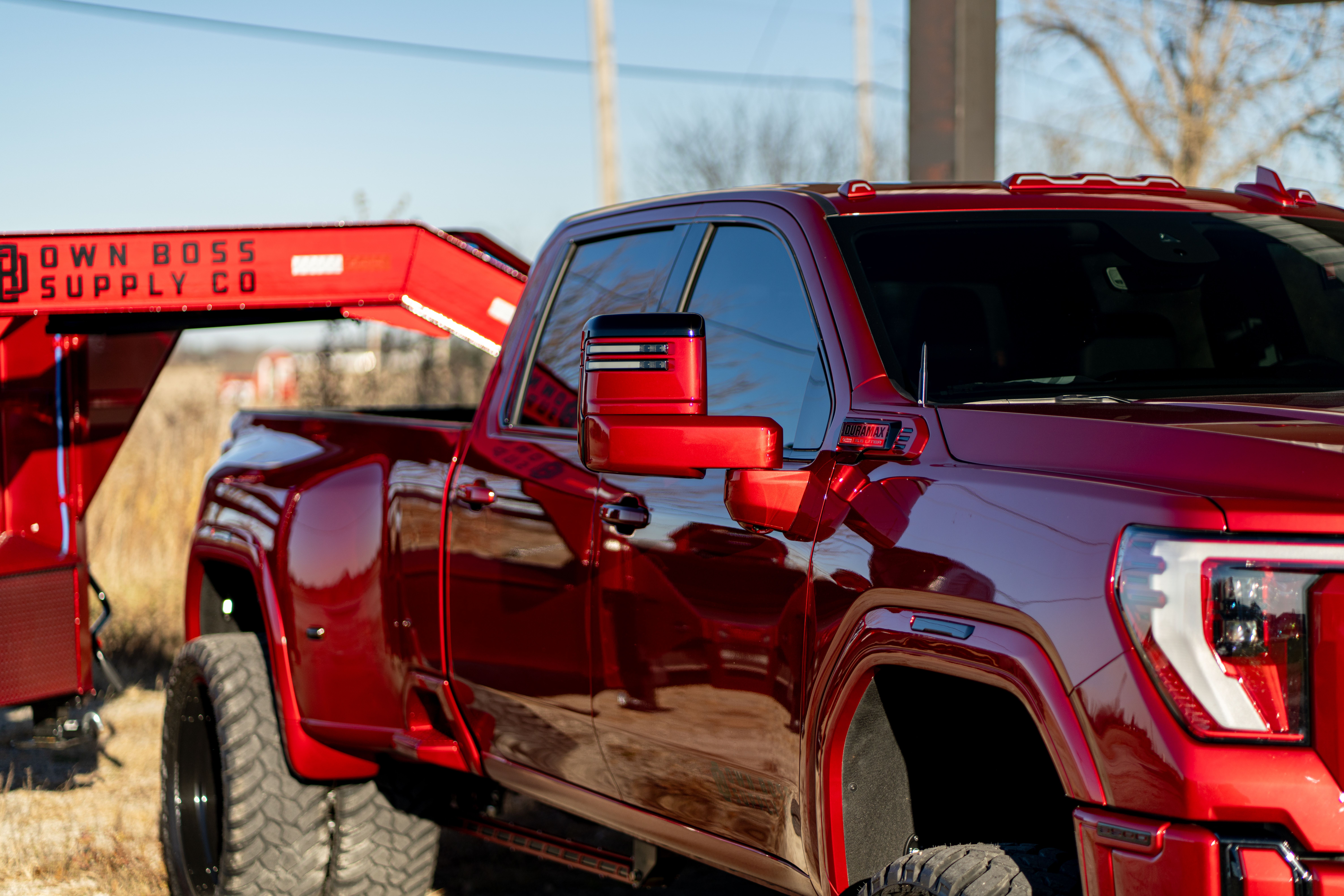 A shiny red dually pickup truck is hitched to a red gooseneck trailer labeled 'OWN BOSS SUPPLY CO'.