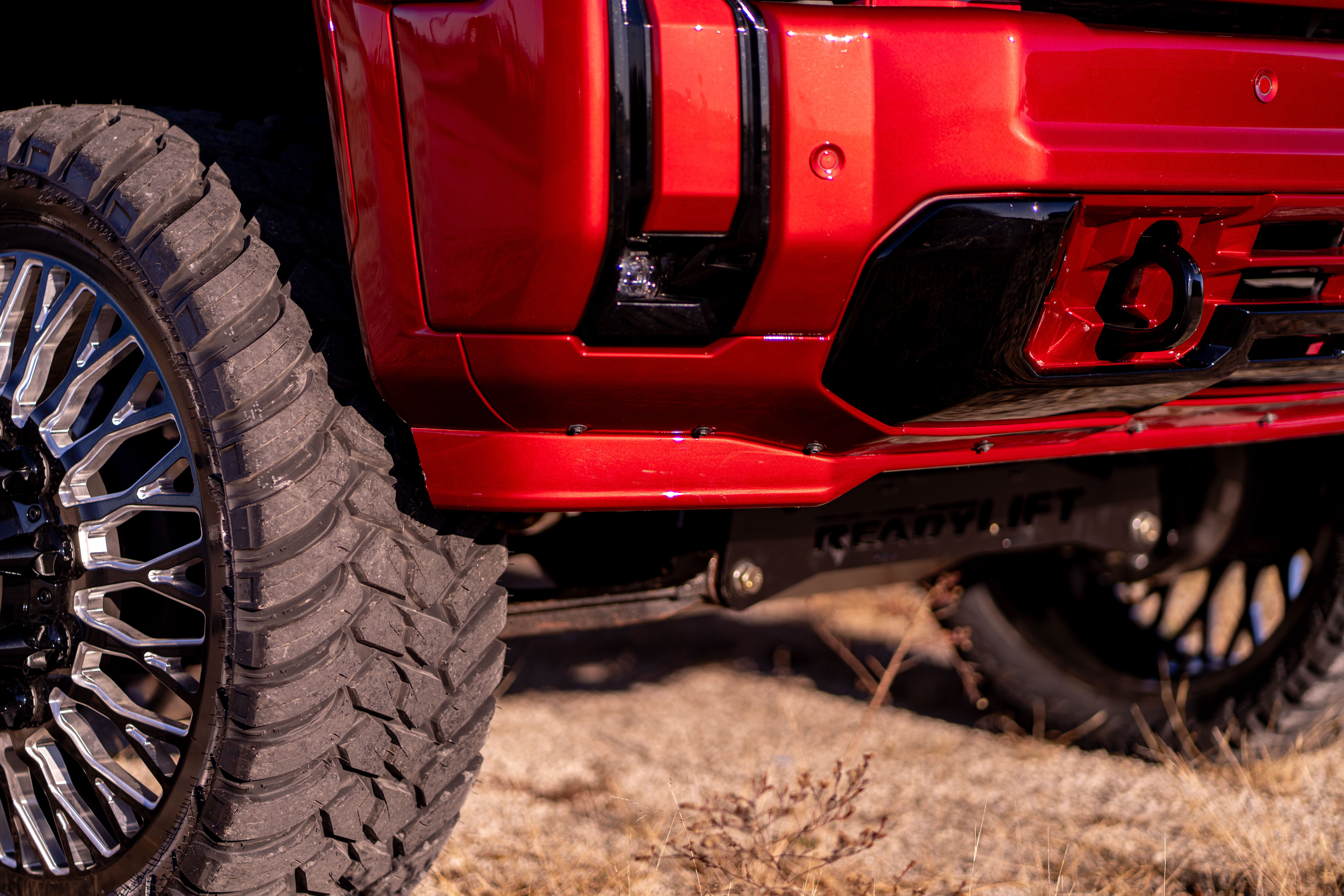 Red pickup truck with large off-road tires and custom black and chrome rims.