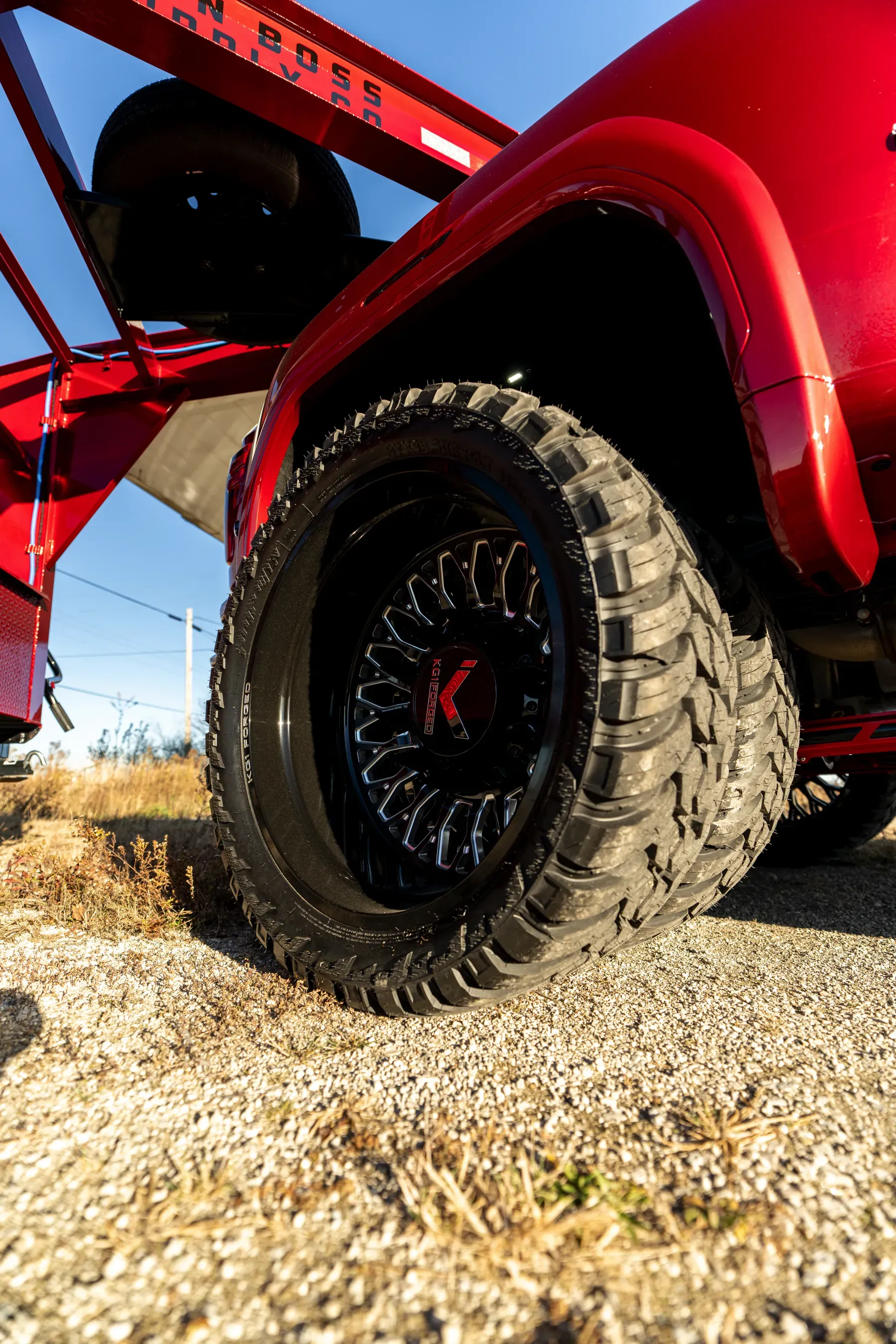 Close-up of a large, aggressive off-road tire on a custom black rim with a red 'K' logo on a red truck.