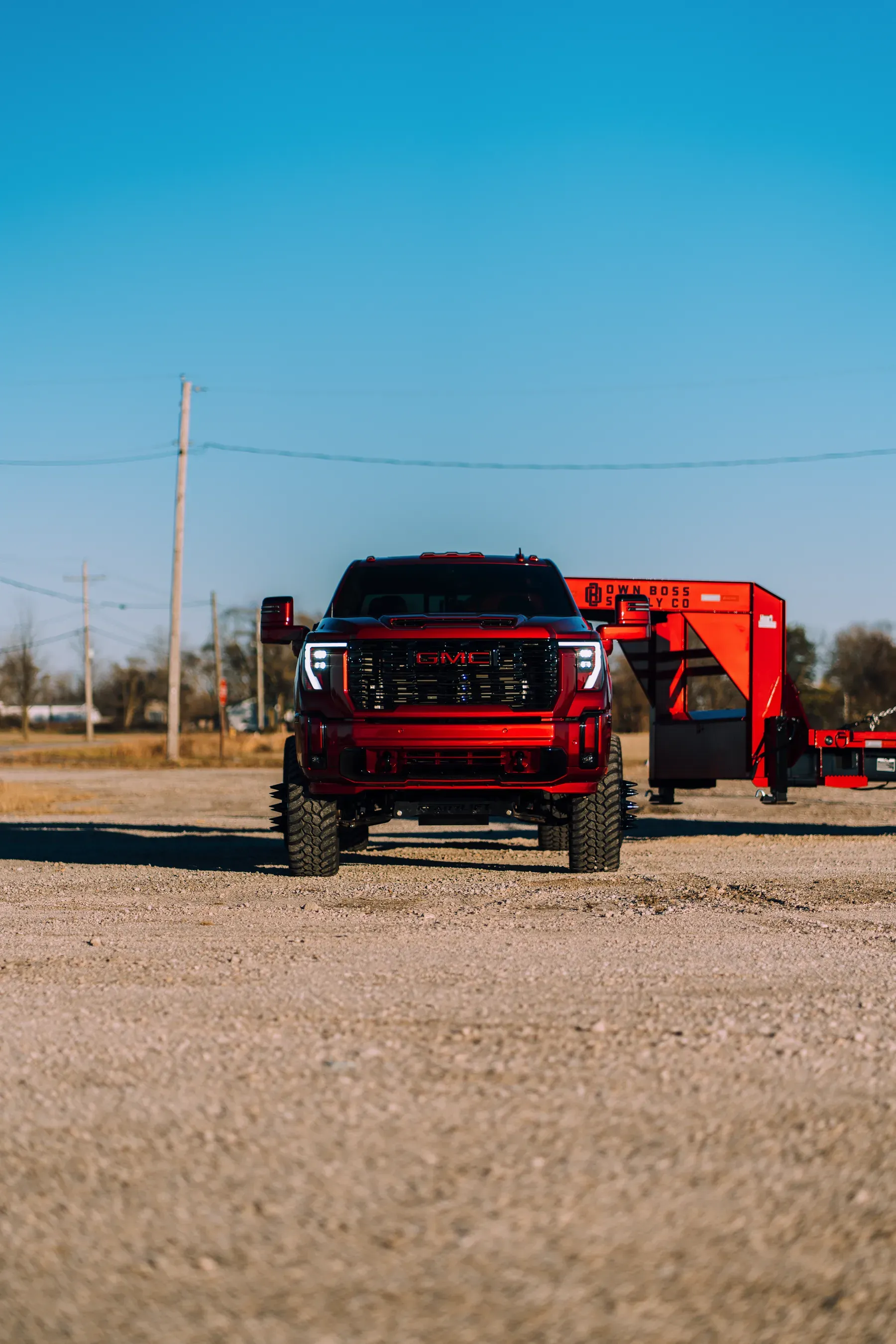 A red Ford F-150 truck with large tires is parked in a gravel lot.
