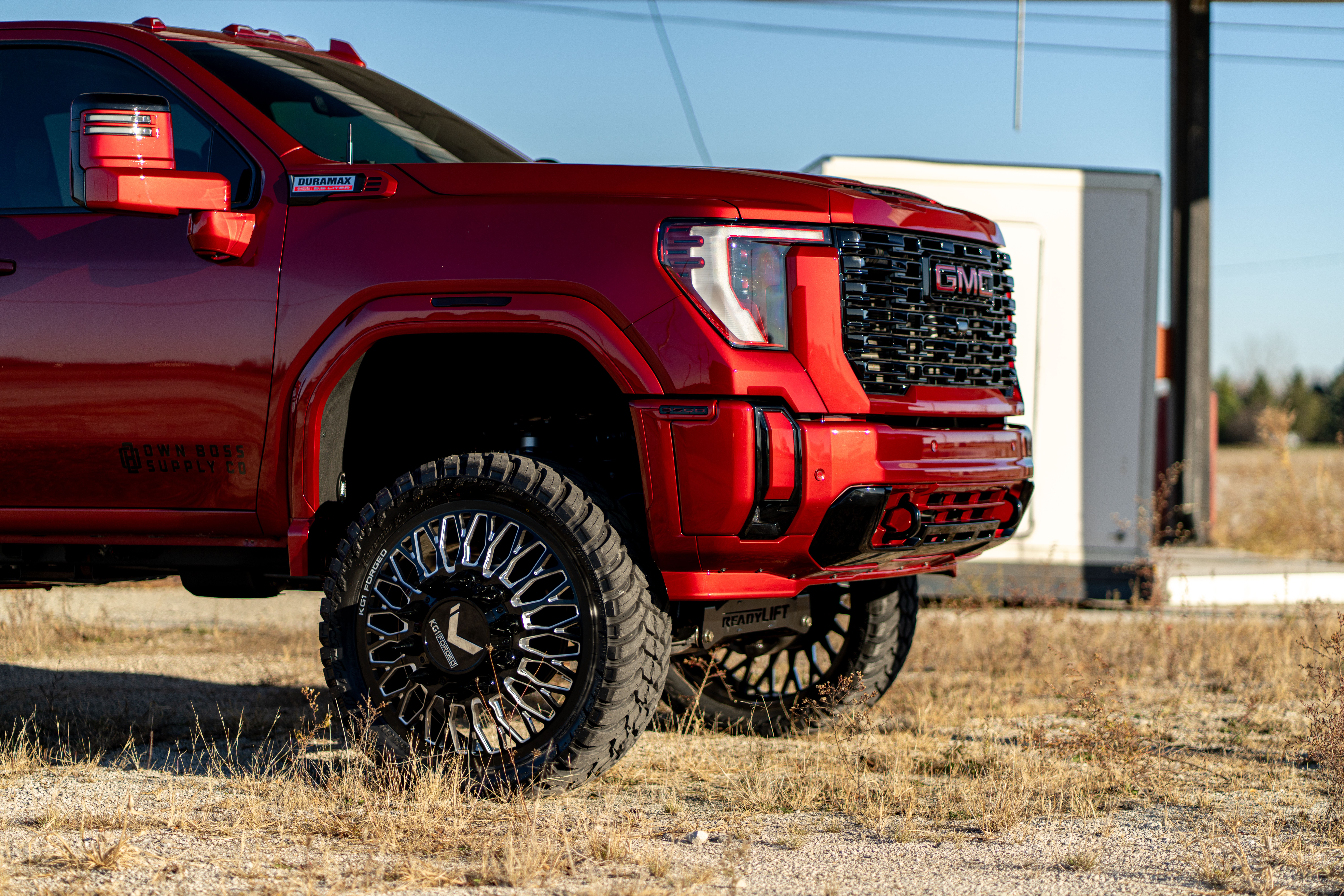 A red lifted GMC Sierra pickup truck with custom black and chrome wheels.