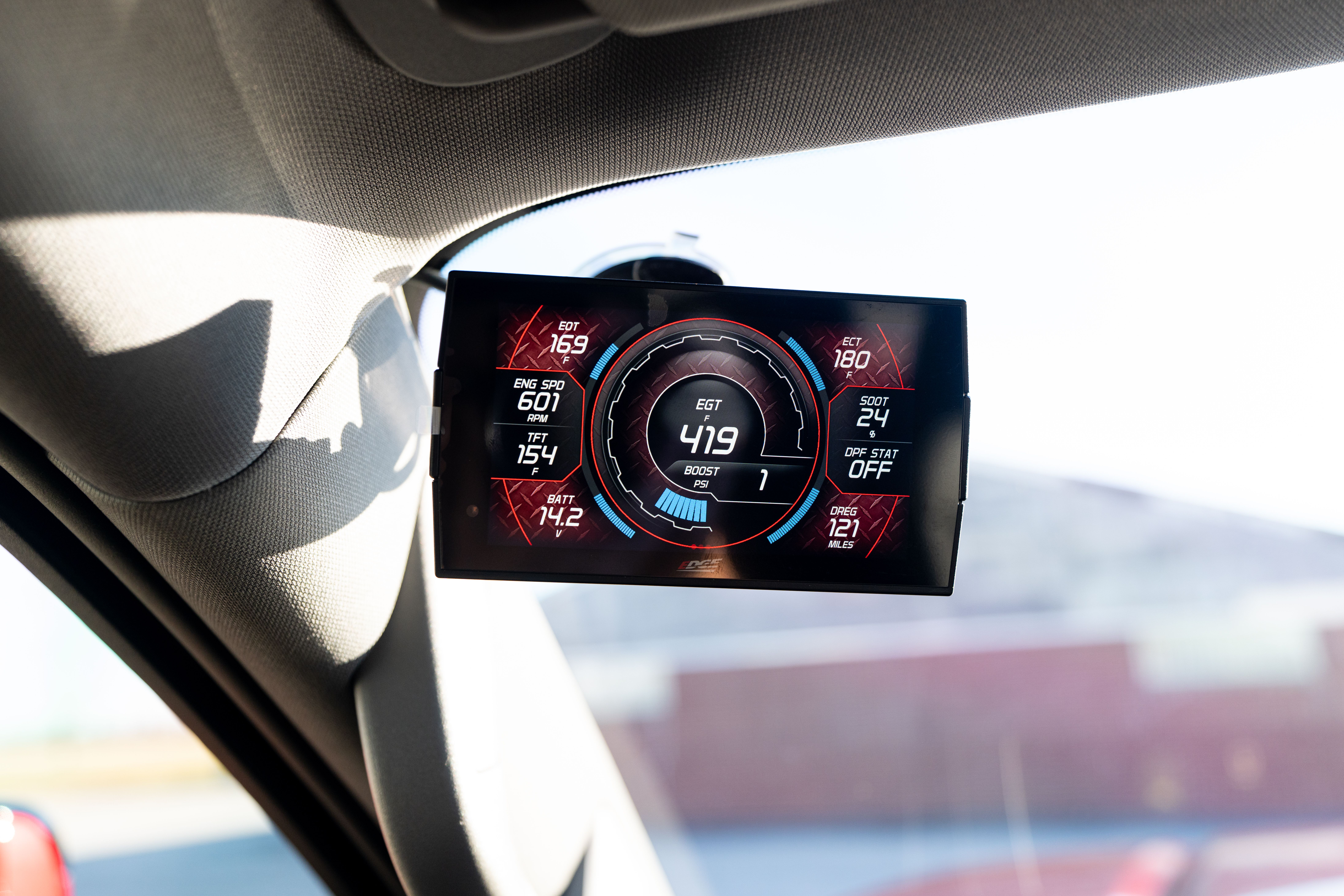 A digital vehicle performance display showing various readings is mounted on a car's dashboard.