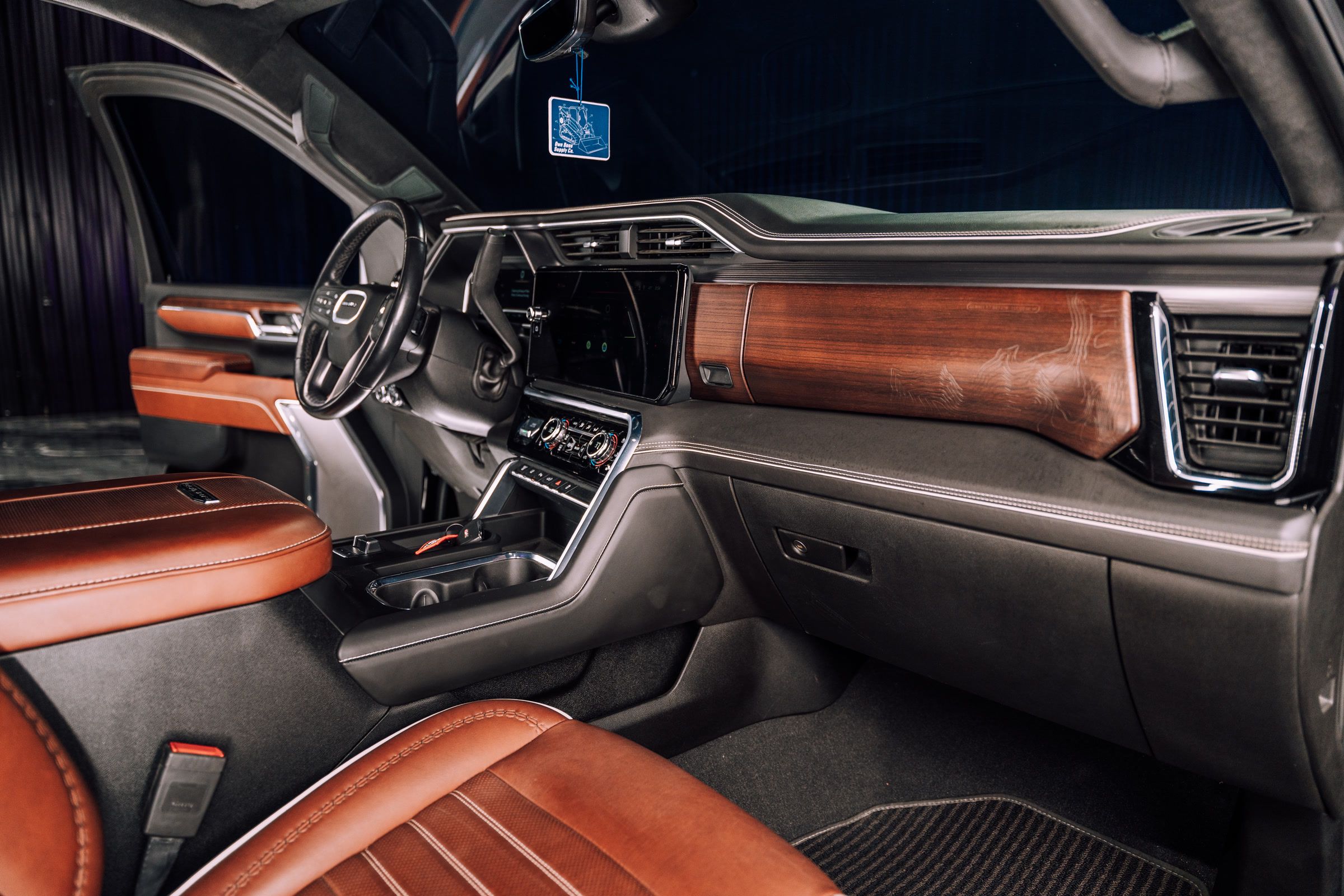 Luxurious car interior with brown leather seats, wood trim dashboard, and large central display.