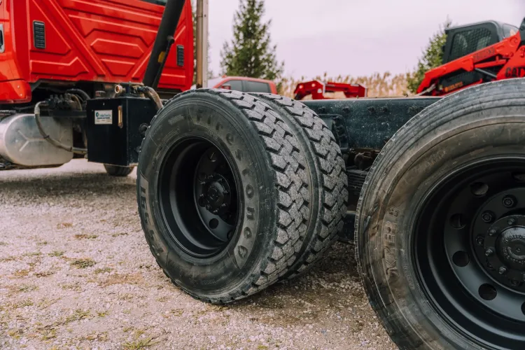 The rear dual wheels and chassis of a red semi-truck parked outdoors.